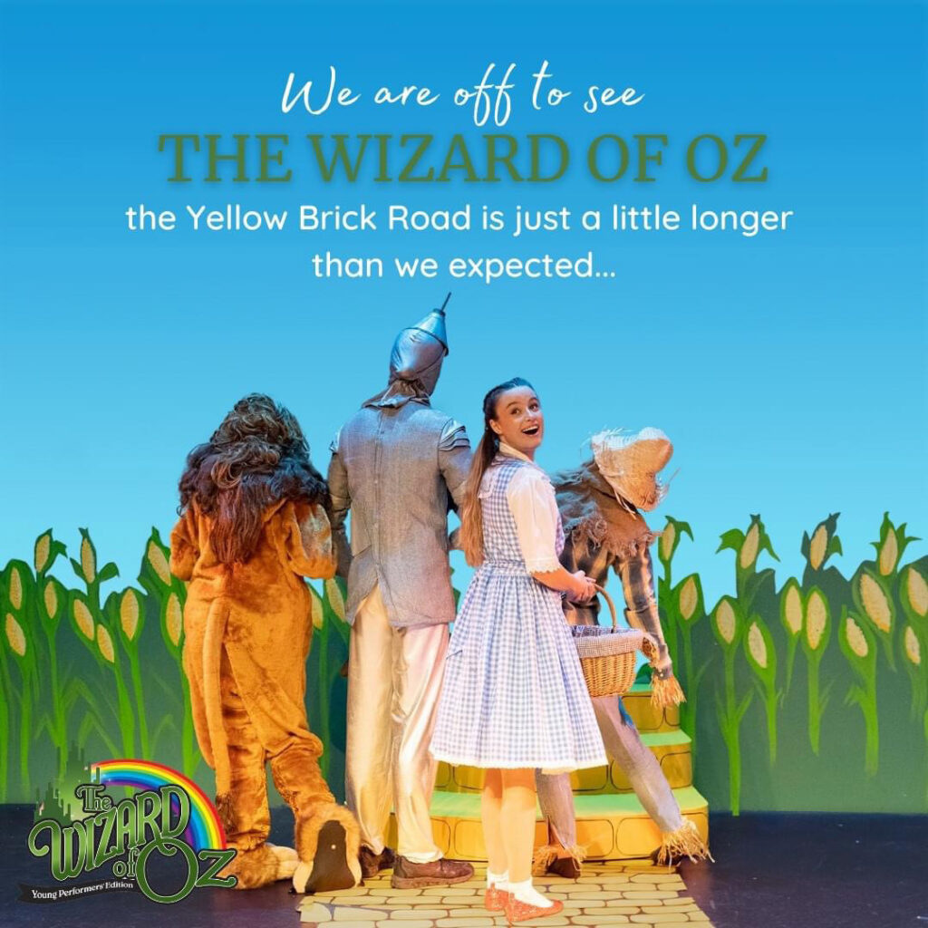 The backs of Dorothy, Lion, Tinman and Scarecow walking on the yellow brick road . Dorothy looking back over her shoulder.