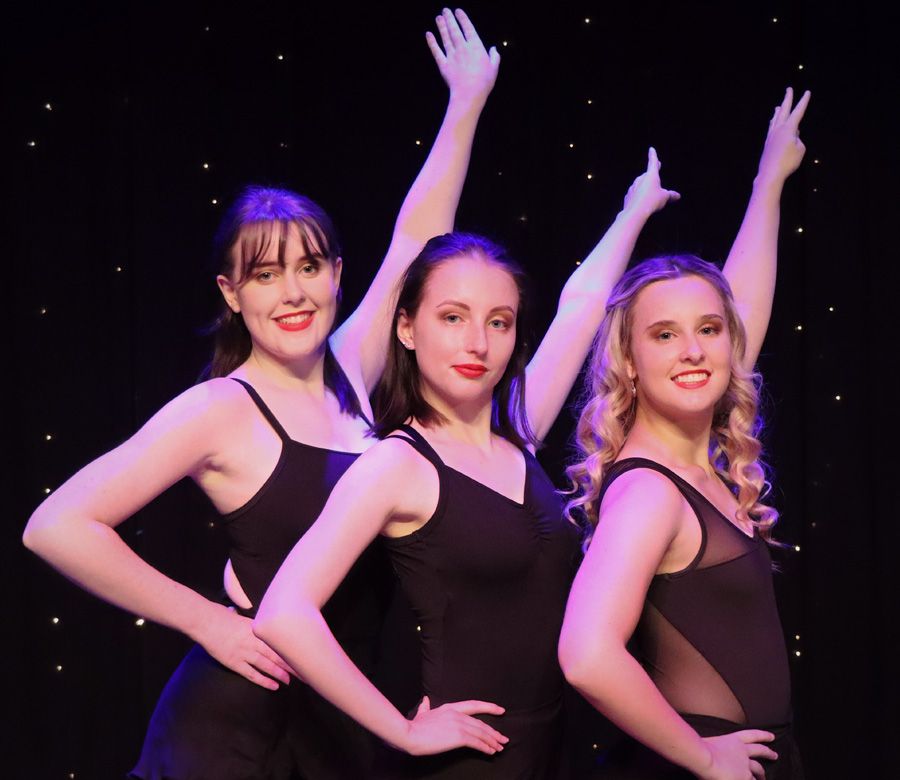 Three dancers holding one arm out straight in unison