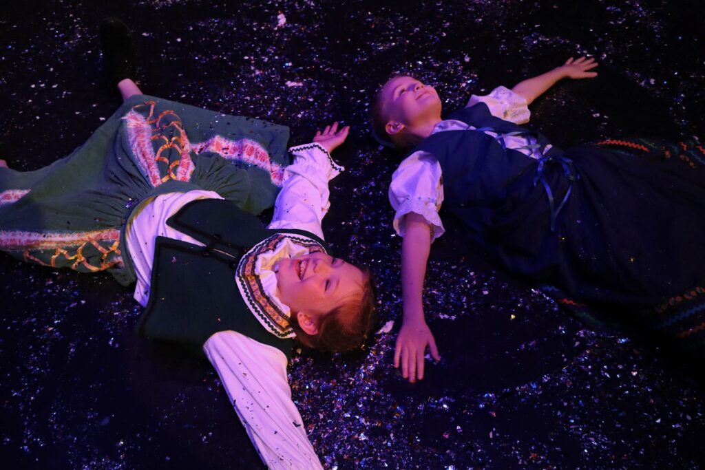 Two girls dressed as Anna and Elsa making snow angels on the floor